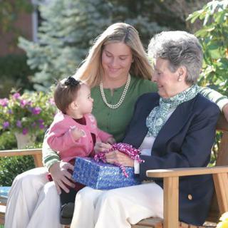 A young woman, a child, and an elderly woman sitting together on a bench in a garden.