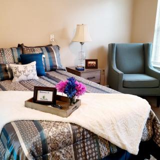 A cozy bedroom with patterned bedding, a decorative tray, and a comfortable armchair by the window.
