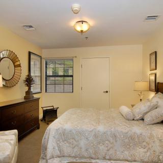 A cozy bedroom with elegant decor, featuring a large bed, mirror, window, and warm lighting.