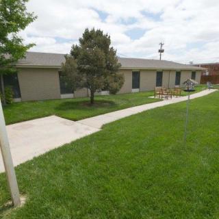A single-story building surrounded by a well-maintained lawn and a paved sidewalk under a cloudy sky.