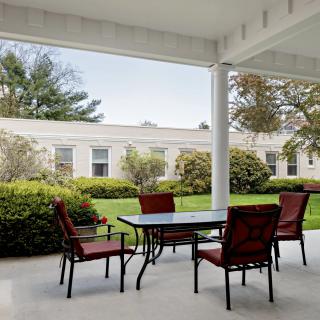 A serene outdoor patio with a table and chairs, surrounded by lush greenery.