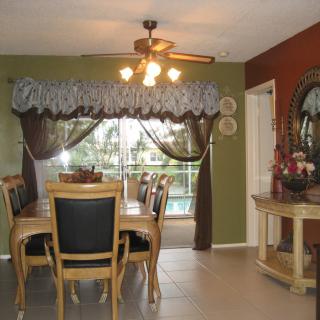 A cozy dining room with a wooden table and chairs, featuring a ceiling fan and large window with a view.
