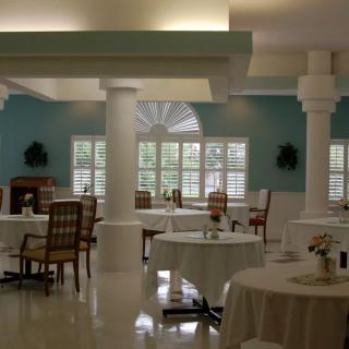 A serene dining area with neatly arranged tables and chairs, illuminated by natural light from large windows.