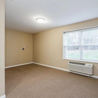 An empty room with beige walls, carpet flooring, a window, and an air conditioner.