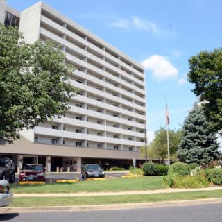 A multi-story apartment building surrounded by greenery under a clear blue sky.