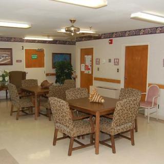 A common area with tables and chairs, decorated with paintings and featuring a ceiling fan.