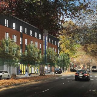 A view of a city street with cars driving by a modern building lined with trees.