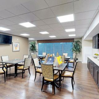 A spacious dining area with multiple tables and chairs, featuring large windows and a television on the wall.