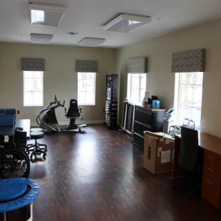 A spacious, empty room featuring office and exercise equipment with ample natural light from large windows.