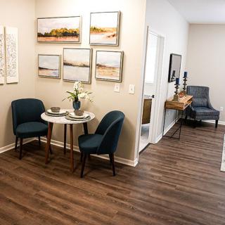 Cozy dining nook with a small table and blue chairs, surrounded by artwork and hardwood flooring.