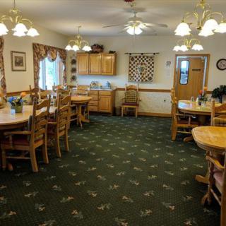 A cozy dining room with wooden tables and chairs, adjacent to a small kitchen area.