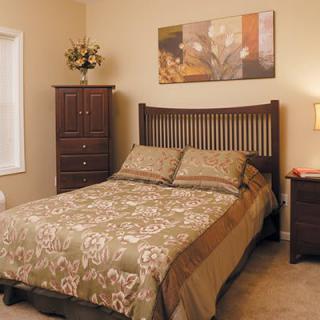 A cozy bedroom with a neatly made bed, wooden furniture, and soft lighting.