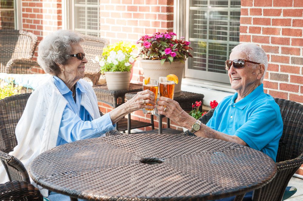 An elderly couple enjoying drinks and toasting on a patio.
