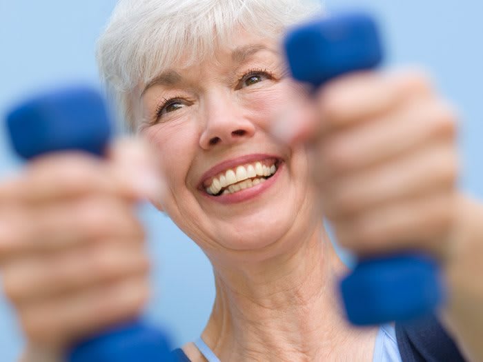 A senior woman smiling while exercising with dumbbells.