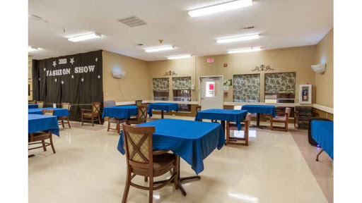 A spacious community room featuring tables with blue tablecloths, suitable for gatherings and activities.