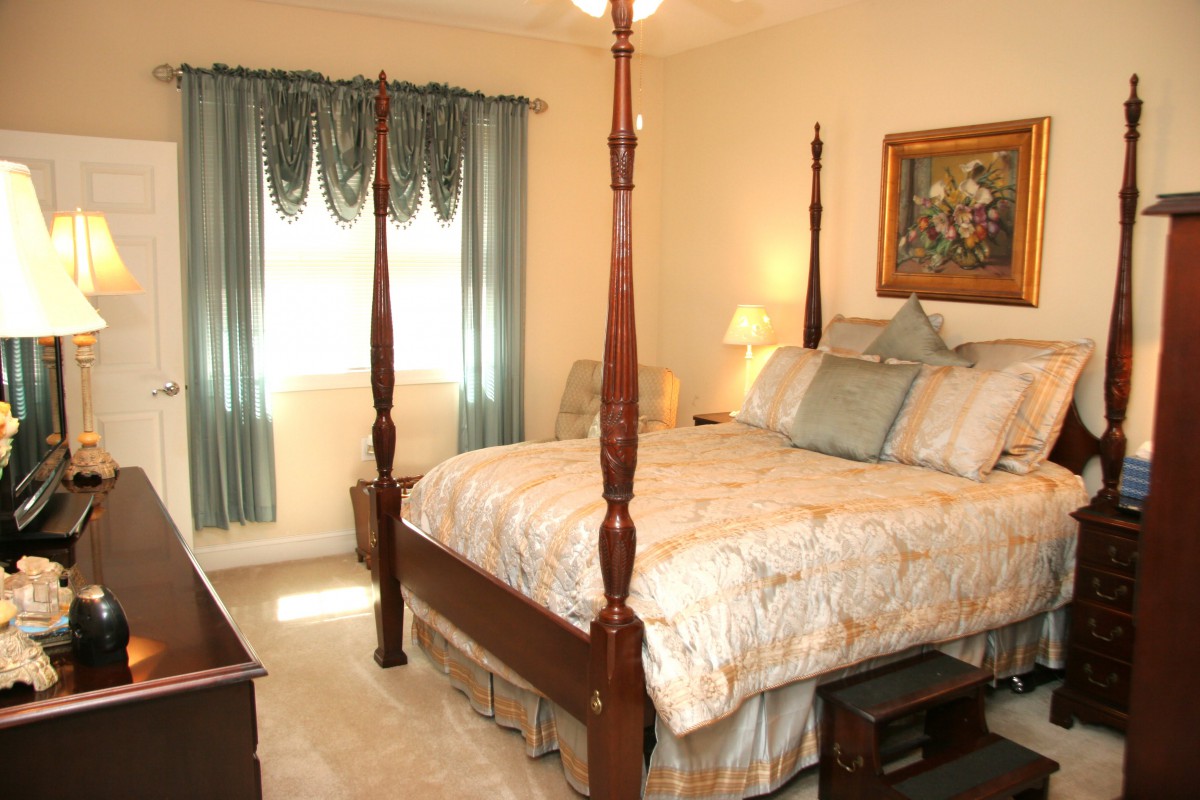 A traditionally decorated bedroom featuring a four poster bed, elegant curtains, and a warmly lit lamp.