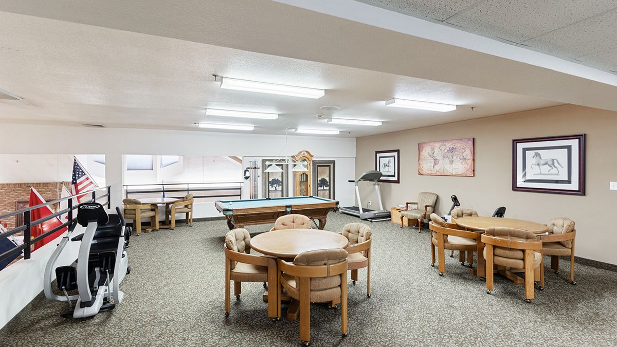 A well-lit recreation room featuring tables and chairs, a billiards table, and exercise equipment.