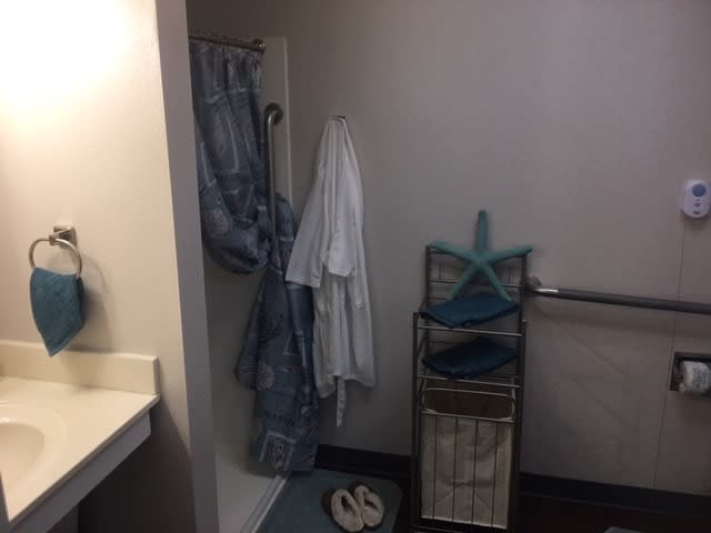 A bathroom corner with a robe and jeans hanging, slippers on the floor, and a hamper with starfish decorations.