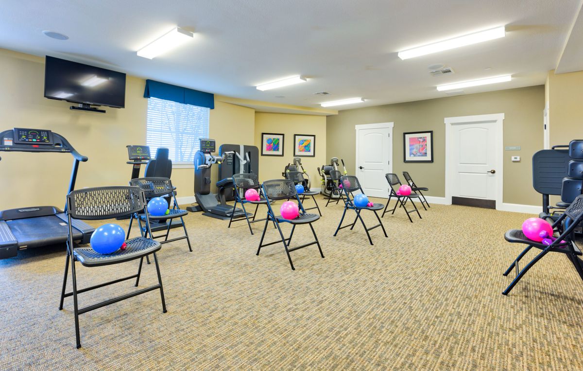 A well-lit exercise room with chairs and fitness balls arranged on a carpeted floor.