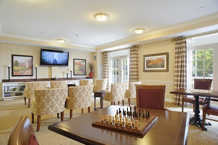 A cozy lounge with a chess board on the table, comfortable chairs, and a television in the background.
