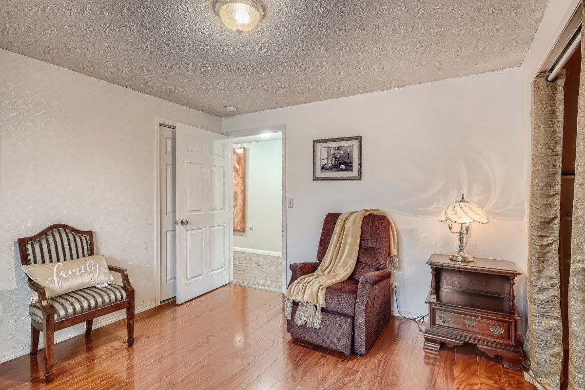 A cozy living room corner featuring an armchair with a throw blanket, accompanied by a side table and lamp, set on a hardwood floor.