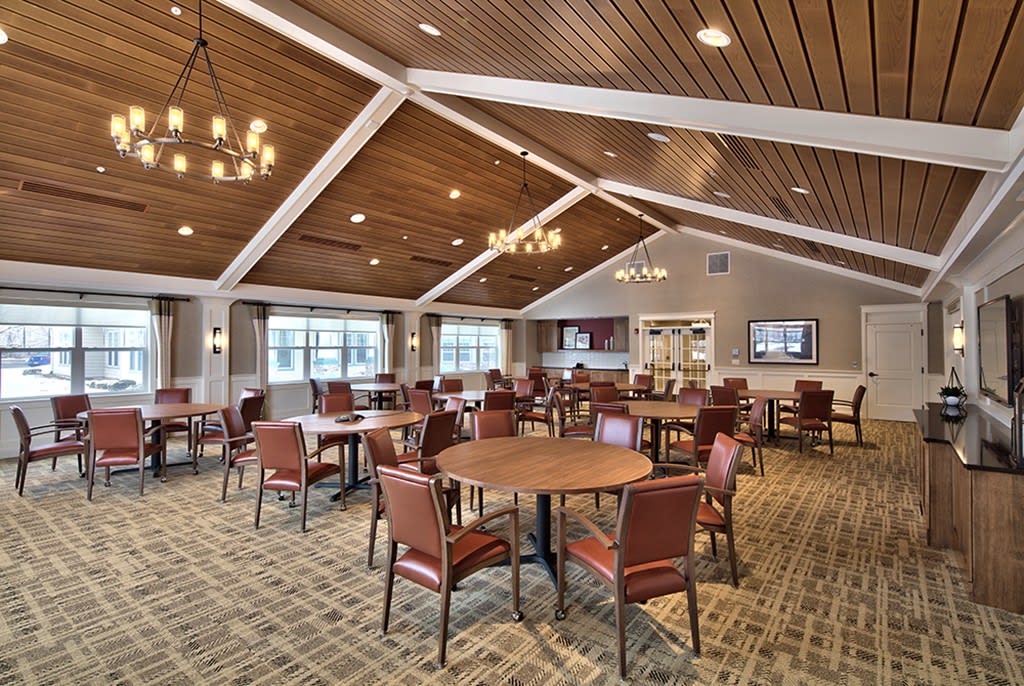 A spacious dining room with wooden ceilings, arranged with round tables and cushioned chairs.