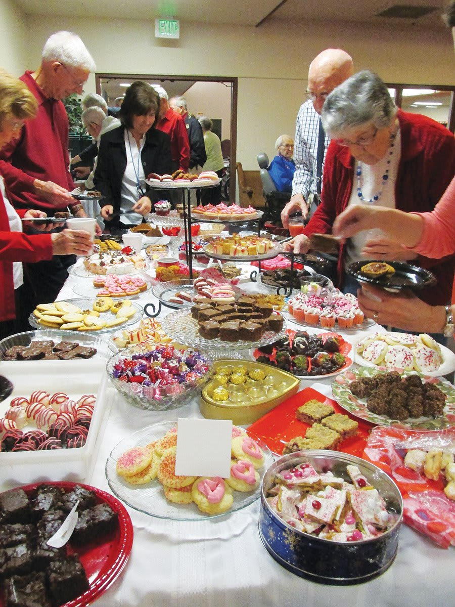 A group of people enjoying a buffet with a variety of desserts and sweets on display.