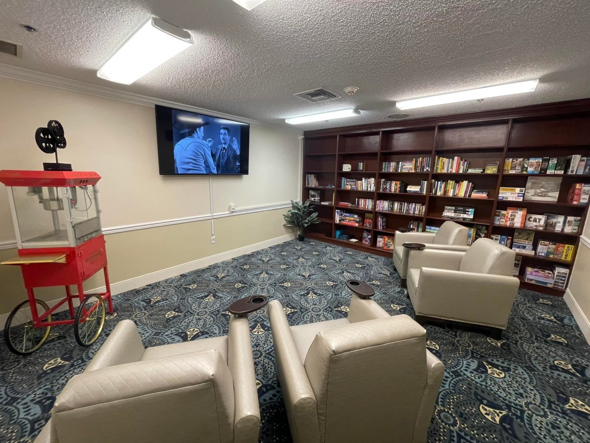 A cozy reading room with bookshelves, comfortable armchairs, a TV, and a popcorn machine.