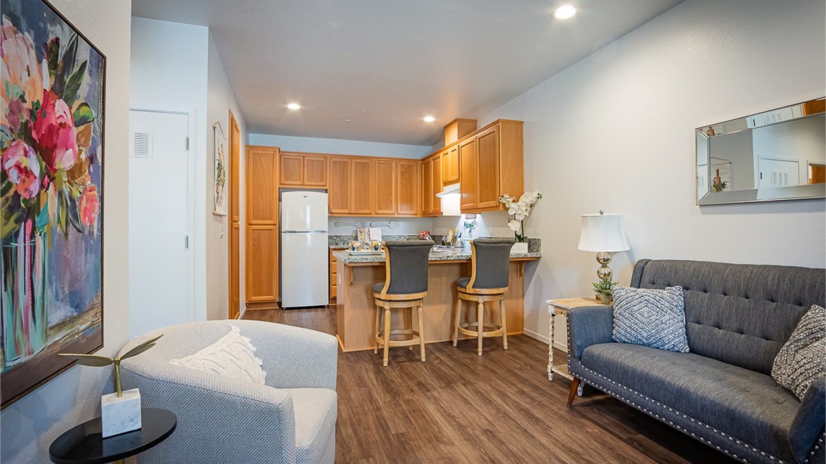 A cozy open floor plan featuring a modern kitchen and living area with wooden cabinetry and bar stools.