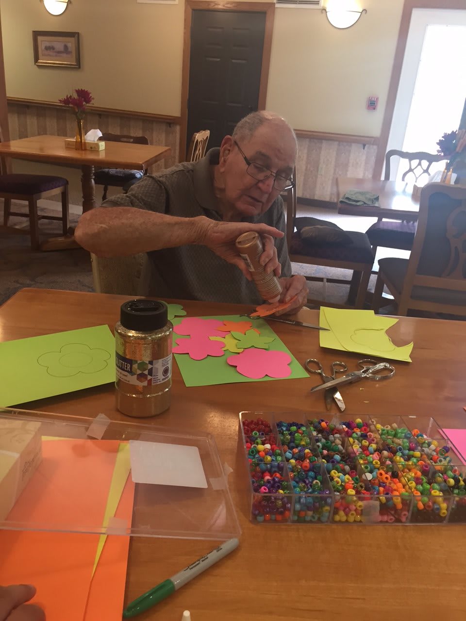 An elderly person engaged in a crafting project with colorful materials and beads.