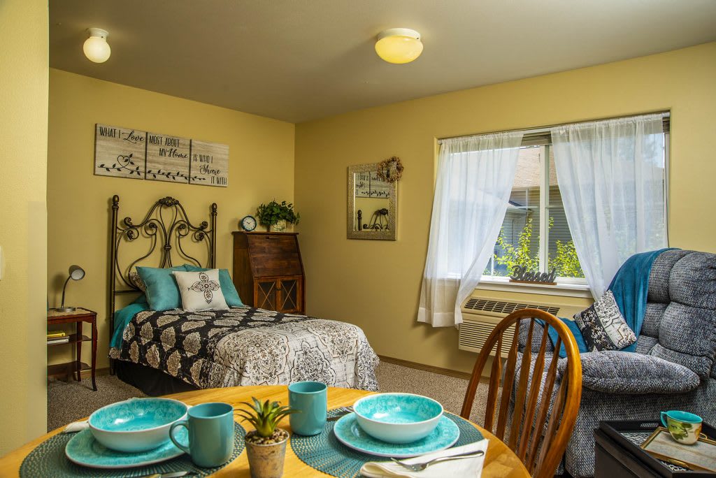 A cozy bedroom with yellow walls, featuring a single bed and a small dining area.