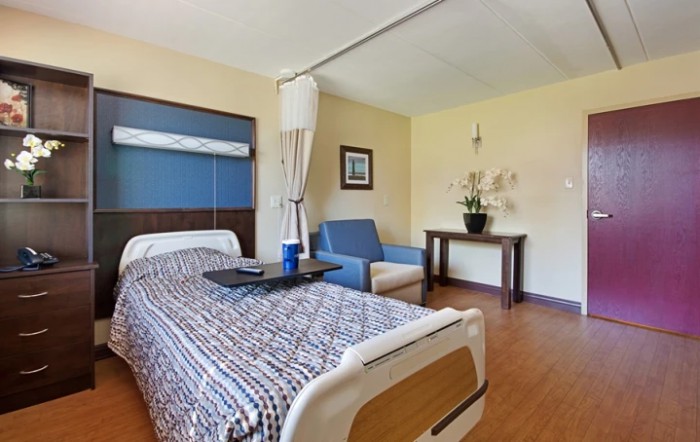 A clean and well-organized hospital room with a bed, seating area, and minimalist decor.