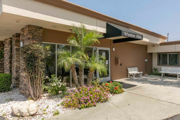 An inviting building entrance with palm trees and colorful flowers.