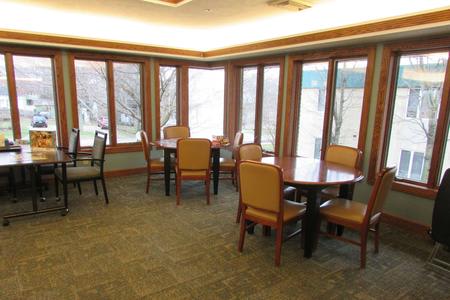 A dining area with several tables and chairs surrounded by large windows allowing natural light in.