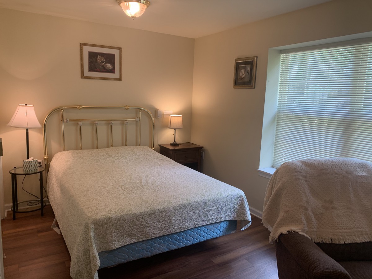A cozy bedroom with a bed, bedside table, and lamp next to a window.