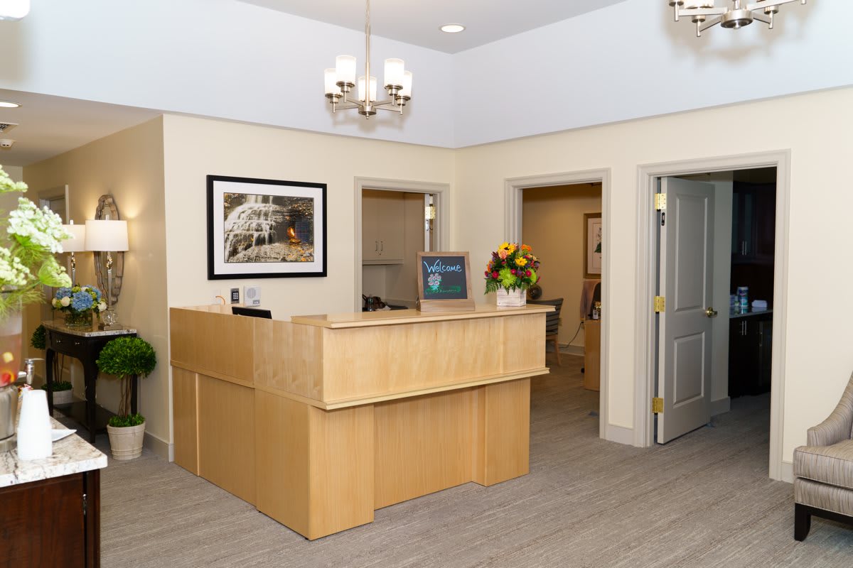 A tidy office reception area with a wooden desk, decorative chandelier, and framed painting.