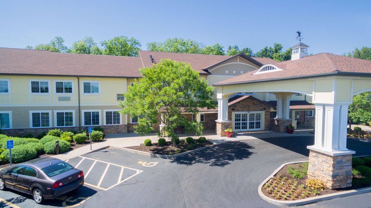 A view of a two-story building with a parking lot and surrounding trees.