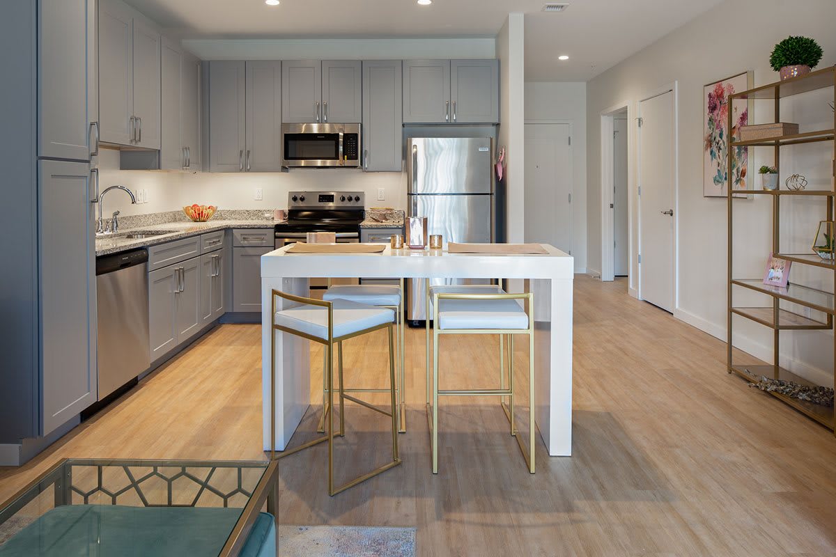 A modern kitchen featuring sleek gray cabinetry, stainless steel appliances, and a small dining area with stylish seating.