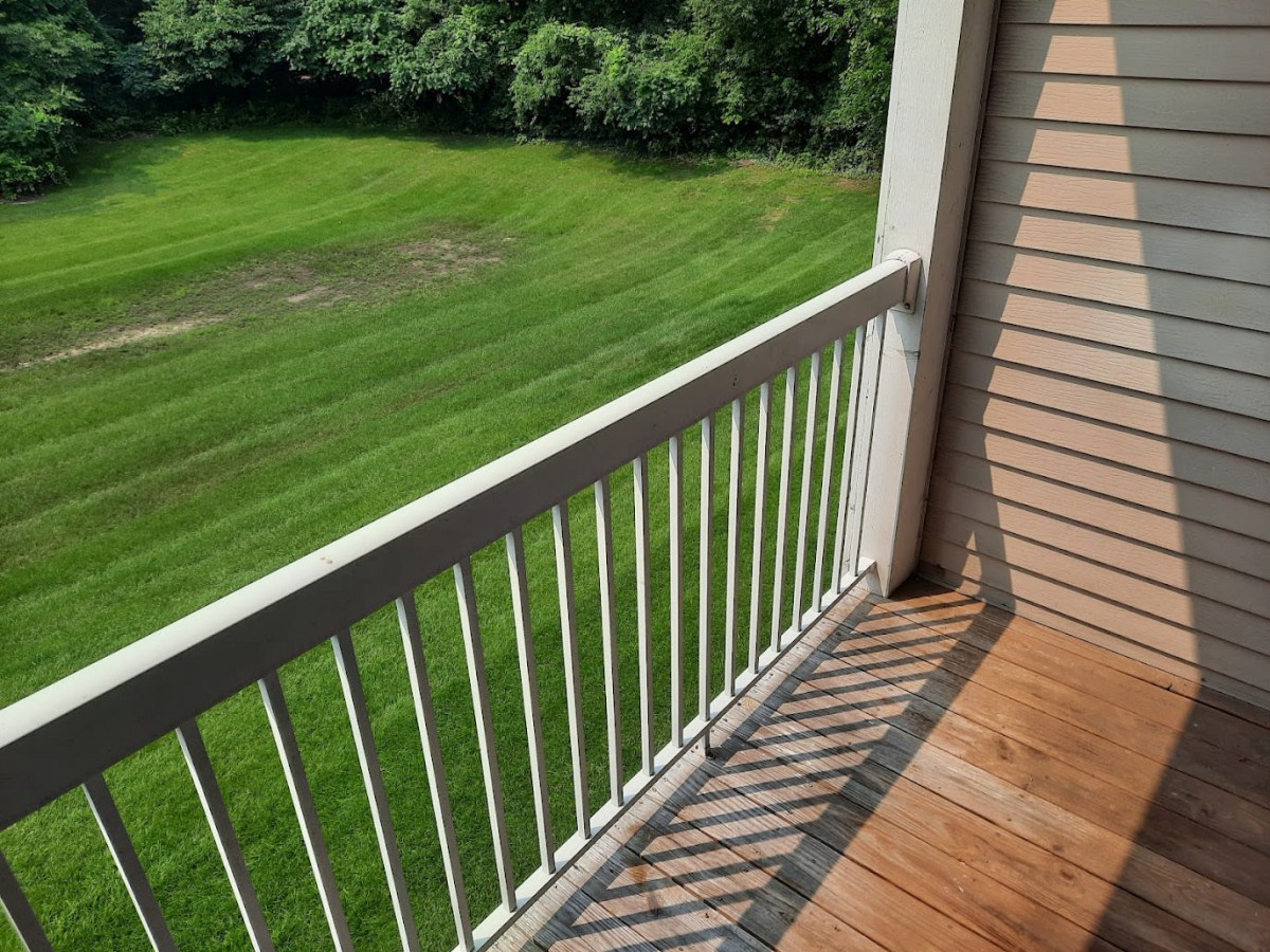 A balcony with white railings overlooking a grassy area on a sunny day.