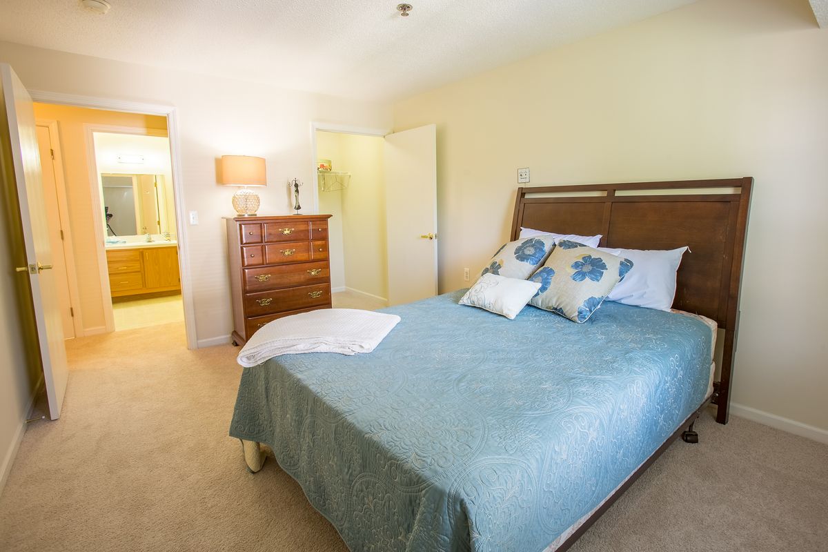 A cozy bedroom with a double bed, wooden dresser, and a lamp.