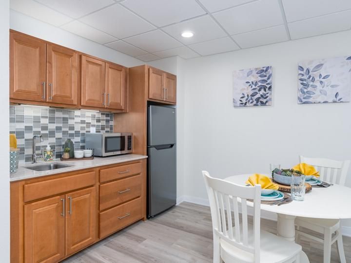A modern kitchen and dining area featuring wooden cabinets, a compact refrigerator, and a neatly set table.