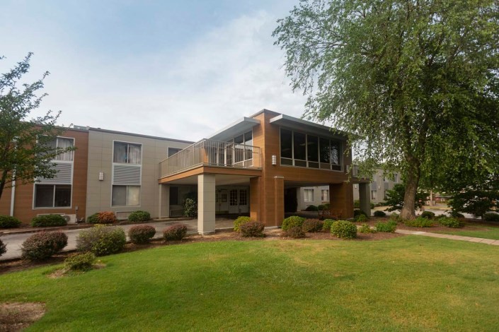 A modern two-story residential building with a well-maintained lawn and surrounding trees.