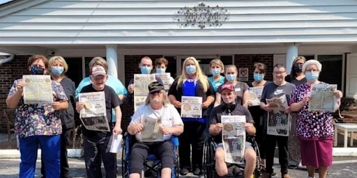 A cheerful group gathers outside holding newspapers, showcasing their camaraderie and community spirit while wearing masks.