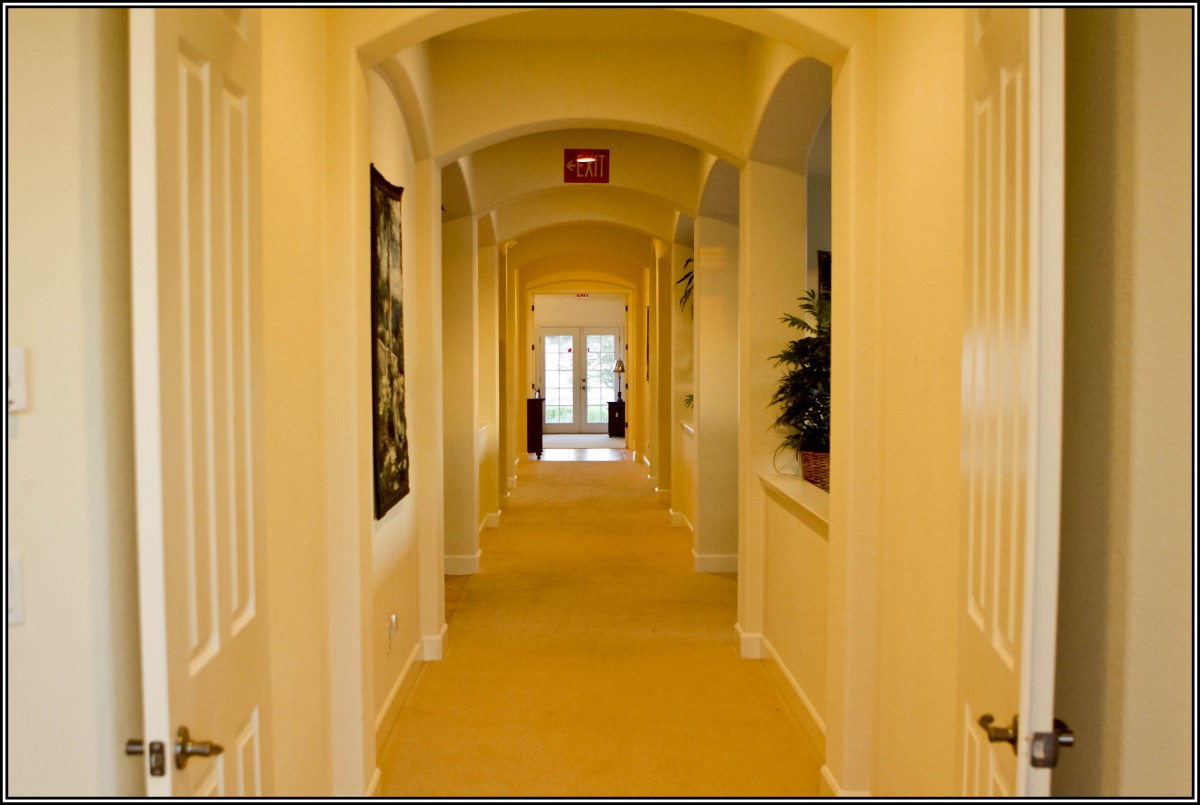 A warmly lit hallway with doors along the sides and artwork on the walls.