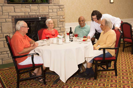 A group of elderly people enjoying a meal together at a restaurant, served by a waiter.