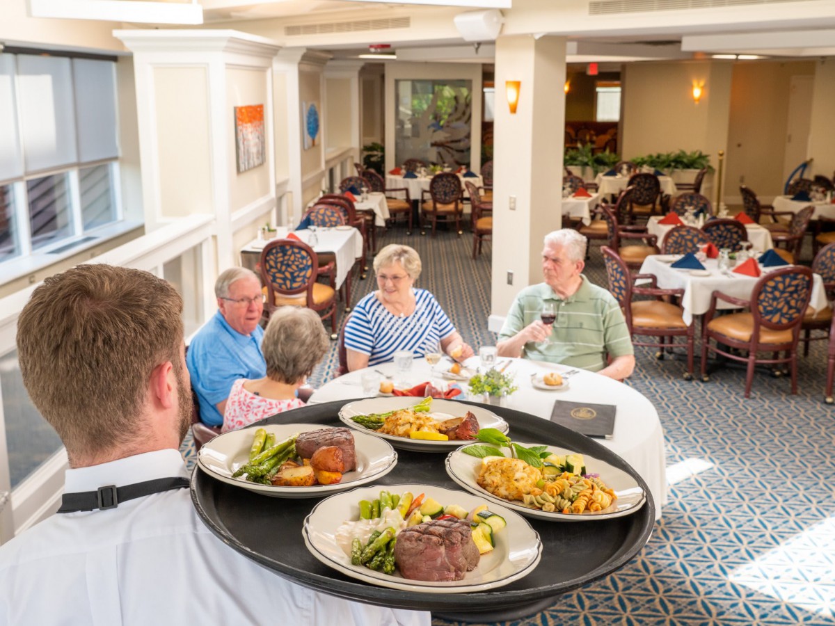 A group of people enjoying a meal in a restaurant with a waiter serving plates of food.