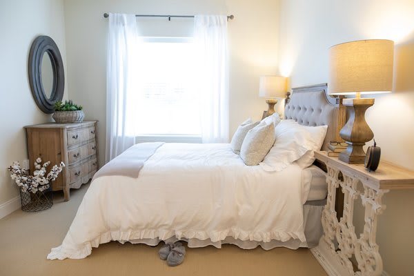 A cozy and well-decorated bedroom with a neatly made bed, two lamps, and a window letting in natural light.