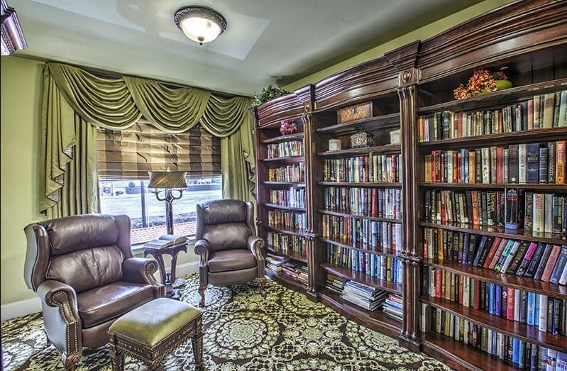 A cozy library and reading room featuring leather chairs, a large wooden bookshelf filled with books, and traditional decor.