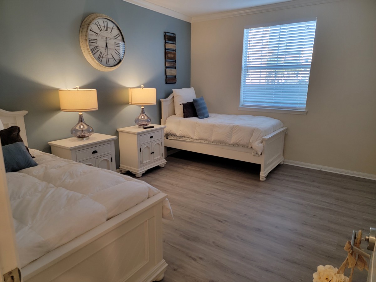 A cozy bedroom featuring twin beds, stylish nightstands with lamps, and a large wall clock.