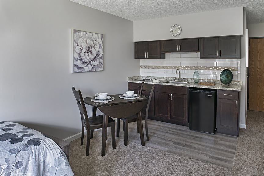 A compact kitchenette with dark cabinets and a small dining area featuring a round table and chairs, complemented by floral artwork on the wall.